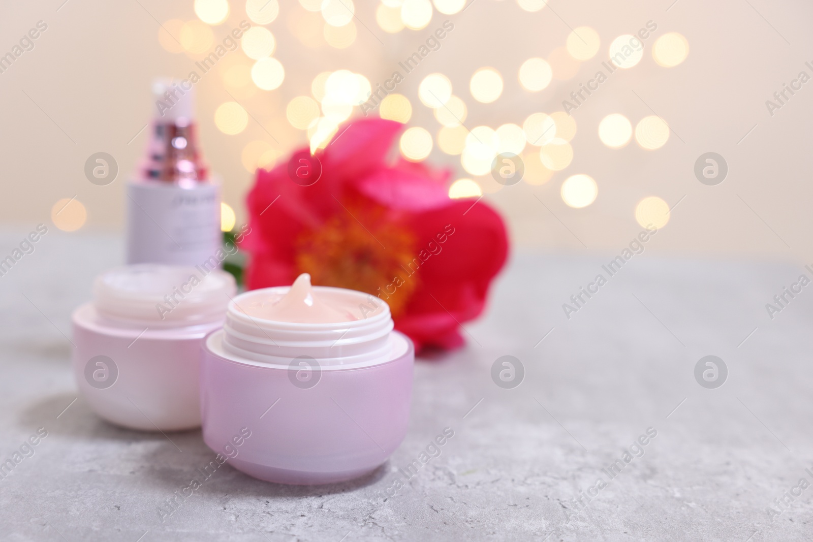 Photo of Set of different cosmetic products and peony flower on gray table against light background with blurred lights. Space for text