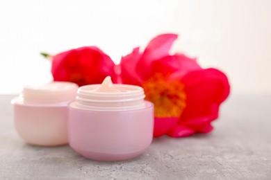 Photo of Jars of creams and peony flower on gray table against light background, closeup