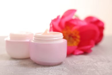 Photo of Jars of creams and peony flower on gray table against light background, closeup