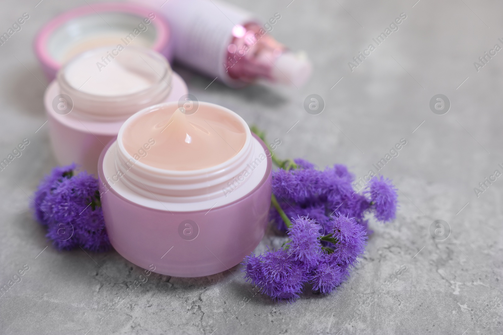 Photo of Set of different cosmetic products and ageratum flowers on gray table, closeup