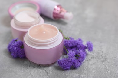 Photo of Set of different cosmetic products and ageratum flowers on gray table, closeup