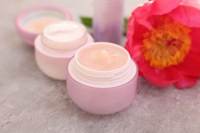 Photo of Set of different cosmetic products and peony flower on gray table, closeup