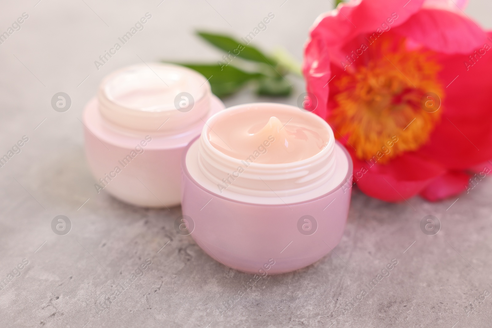 Photo of Jars of creams and peony flower on gray table, closeup