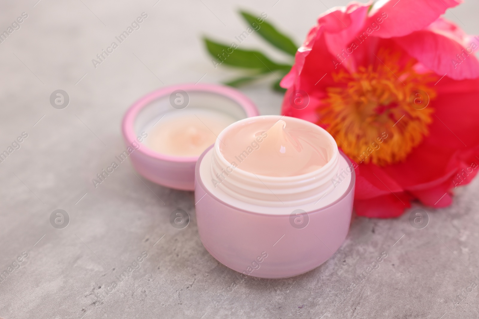 Photo of Jar of cream and peony flower on gray table, closeup