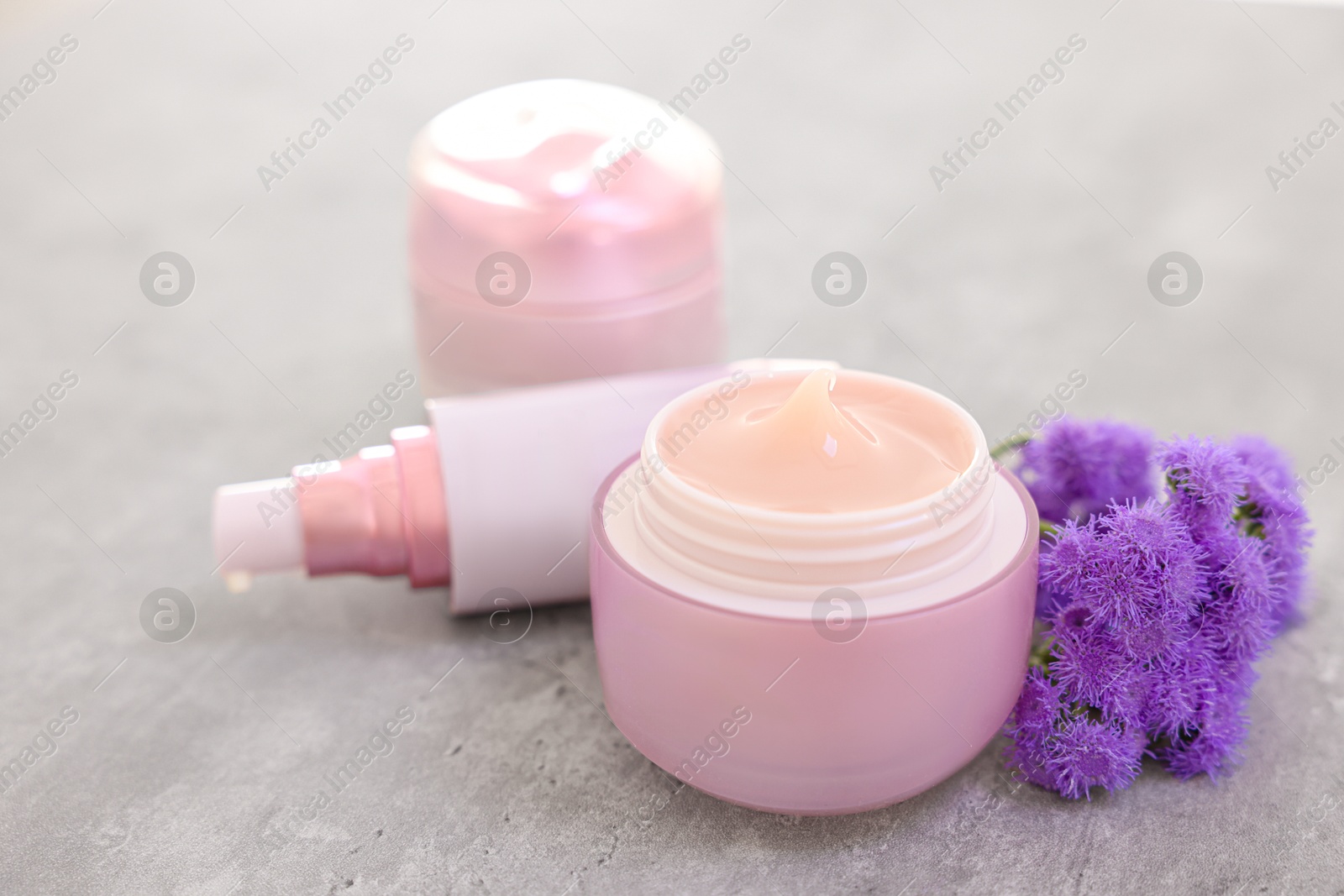 Photo of Set of different cosmetic products and ageratum flowers on gray table, closeup