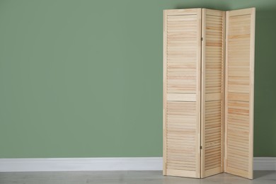 Photo of Wooden folding screen near green wall indoors, space for text