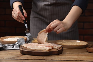 Photo of Woman making schnitzel at wooden table, closeup