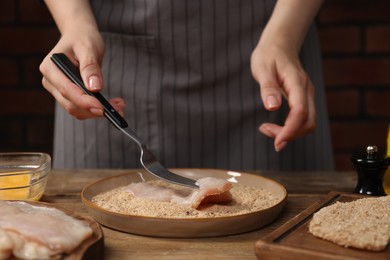 Photo of Woman making schnitzel at wooden table, closeup