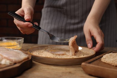 Photo of Woman making schnitzel at wooden table, closeup