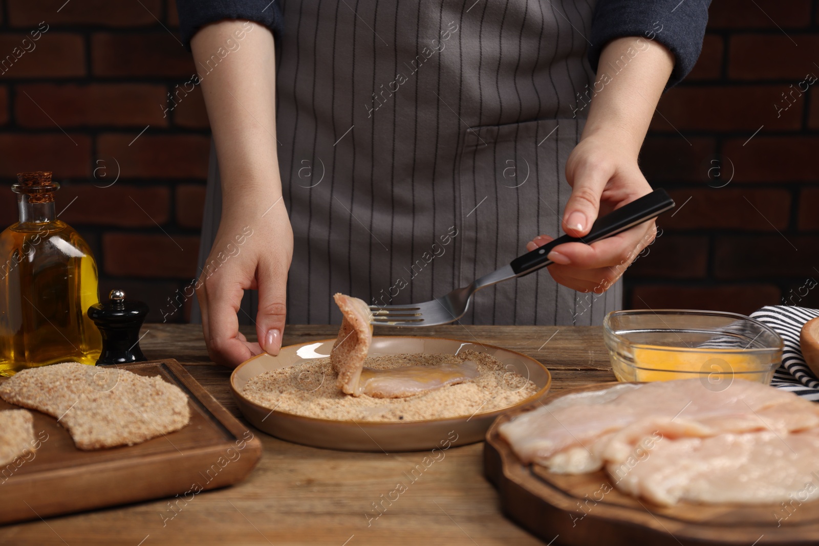 Photo of Woman making schnitzel at wooden table, closeup