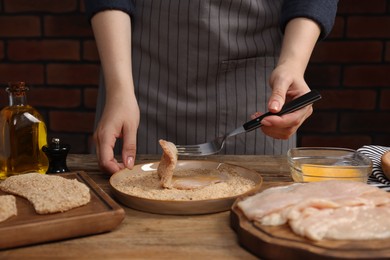 Photo of Woman making schnitzel at wooden table, closeup