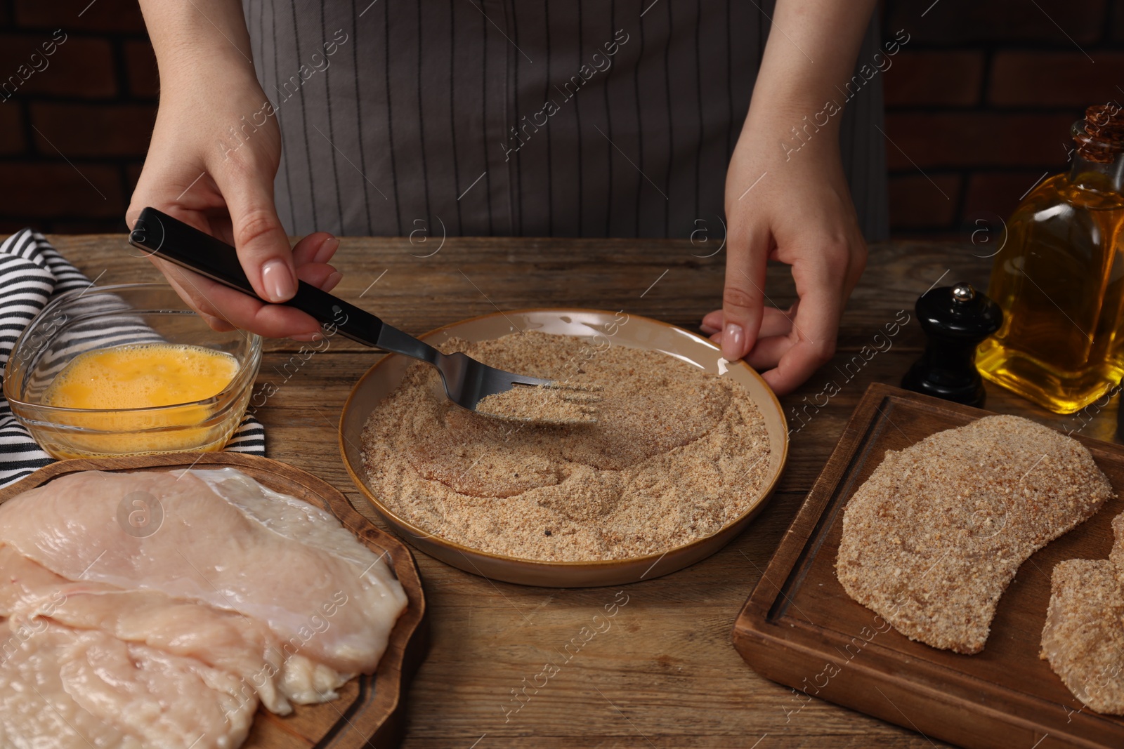 Photo of Woman making schnitzel at wooden table, closeup