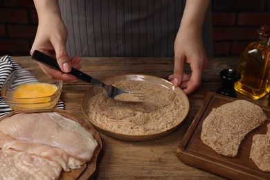 Woman making schnitzel at wooden table, closeup