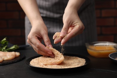 Photo of Woman making schnitzel at black table, closeup