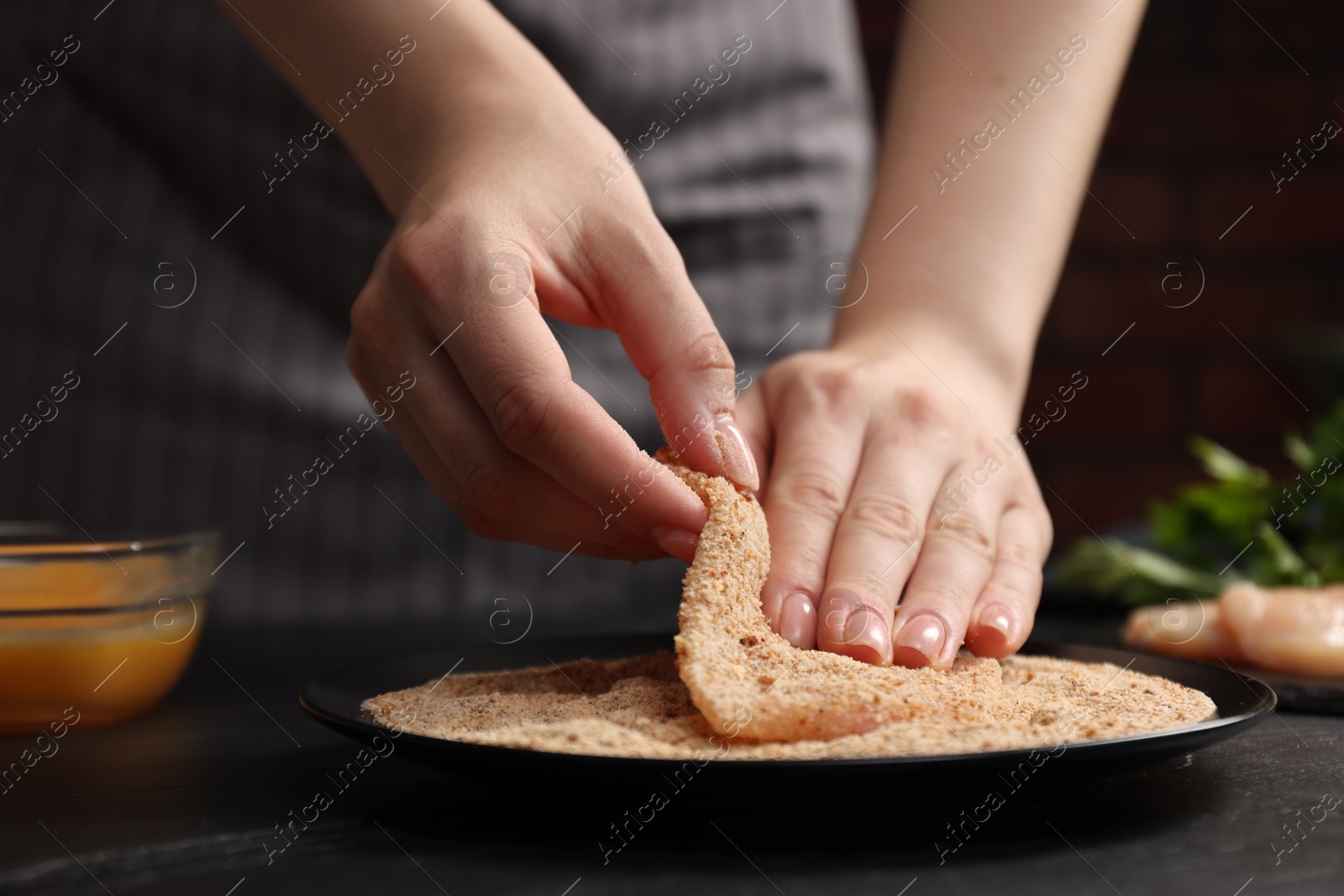 Photo of Woman making schnitzel at black table, closeup