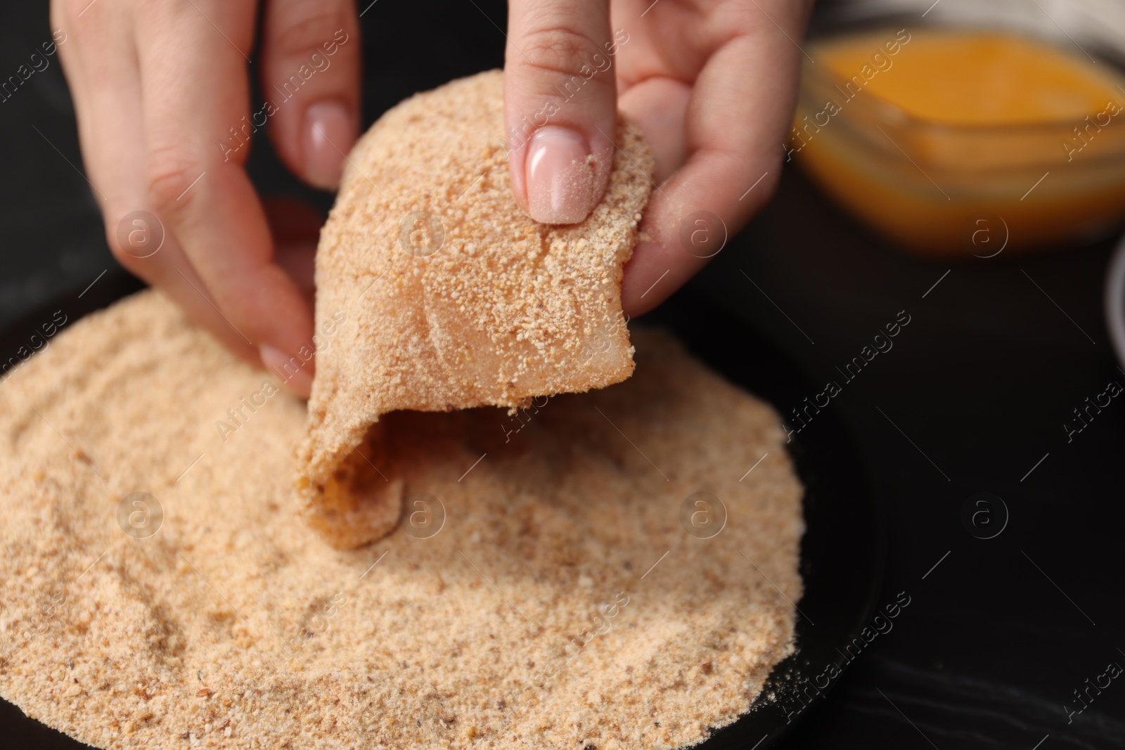 Photo of Woman making schnitzel at black table, closeup