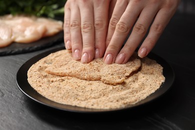 Photo of Woman making schnitzel at black table, closeup