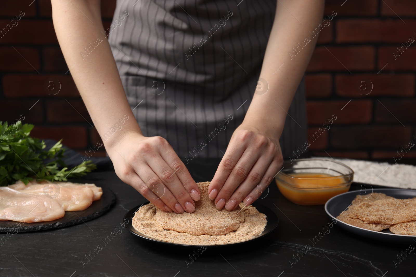 Photo of Woman making schnitzel at black table, closeup