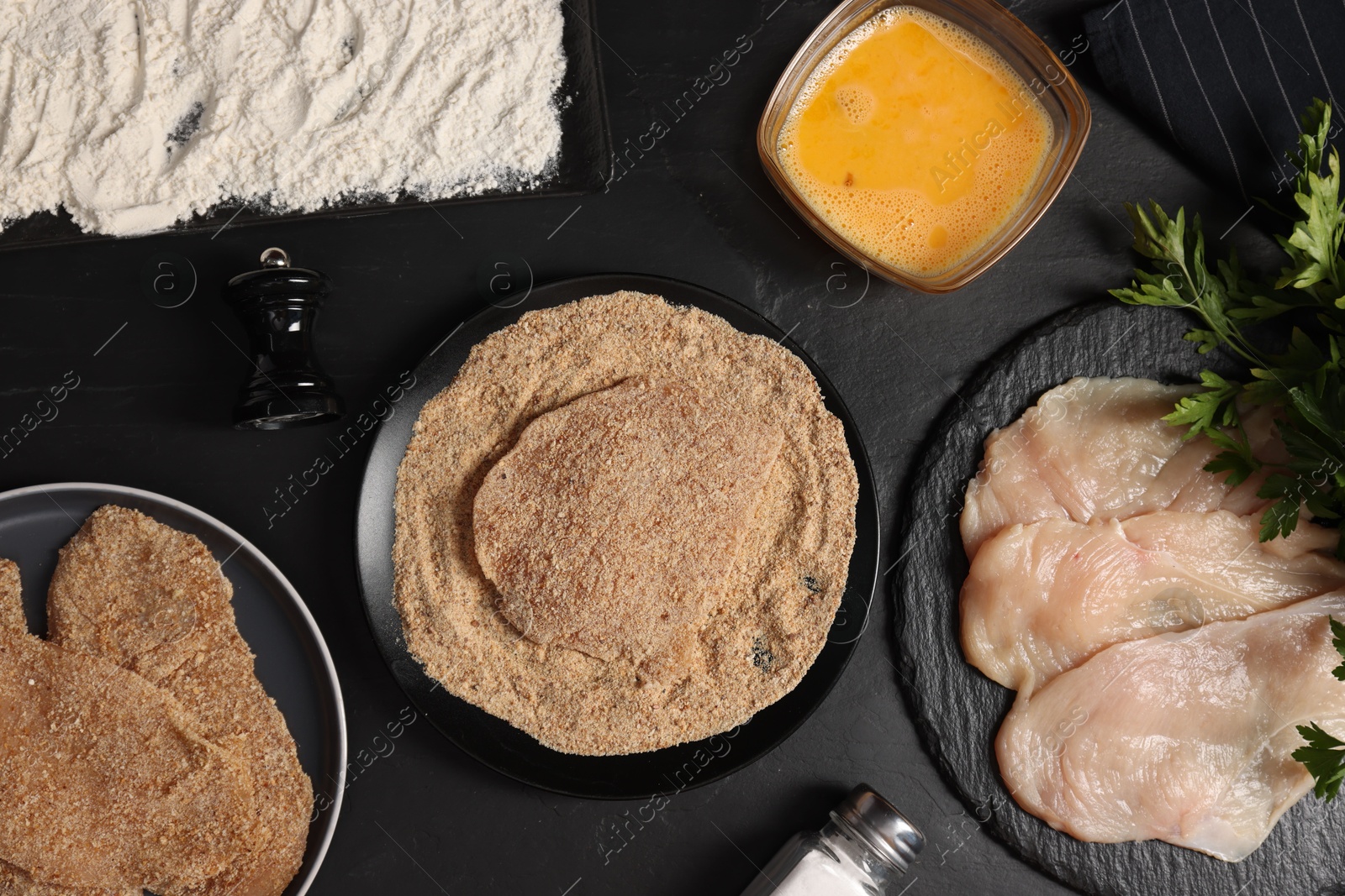 Photo of Making schnitzels. Raw meat and other ingredients on black table, flat lay