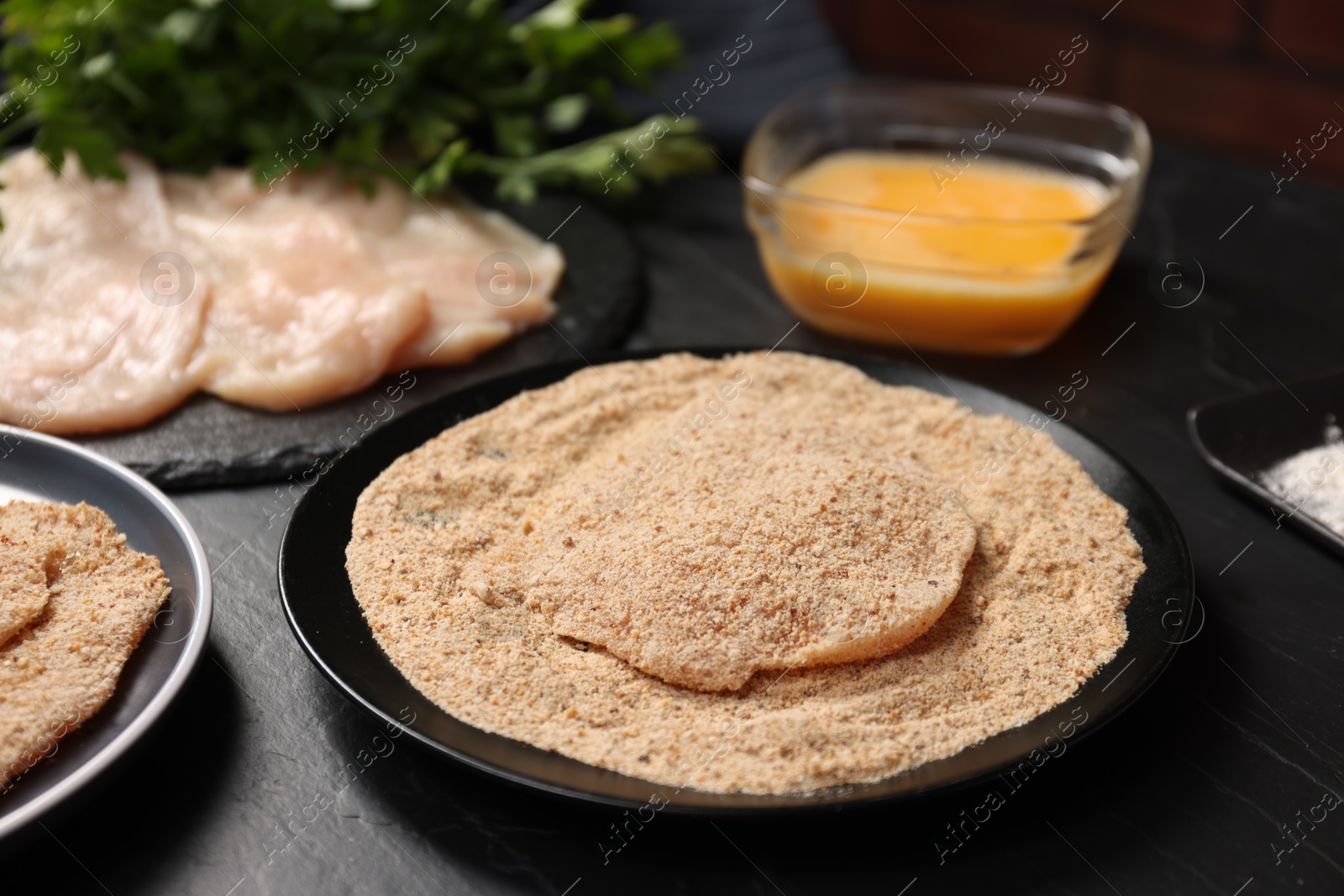 Photo of Making schnitzels. Raw meat and other ingredients on black table, closeup