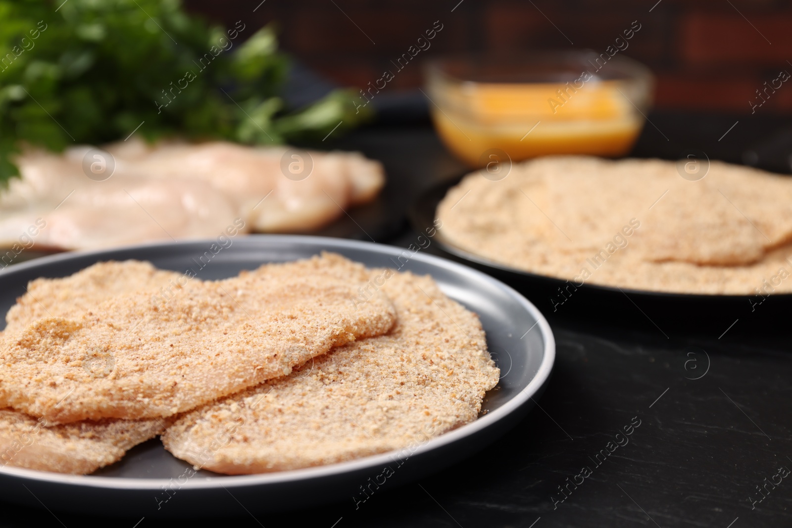 Photo of Making schnitzels. Raw meat and other ingredients on black table, closeup