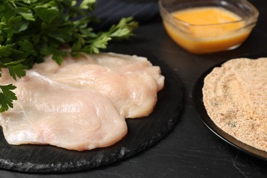 Photo of Making schnitzels. Raw meat and other ingredients on black table, closeup