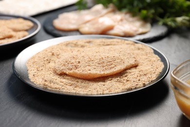 Photo of Making schnitzels. Raw meat and other ingredients on black table, closeup