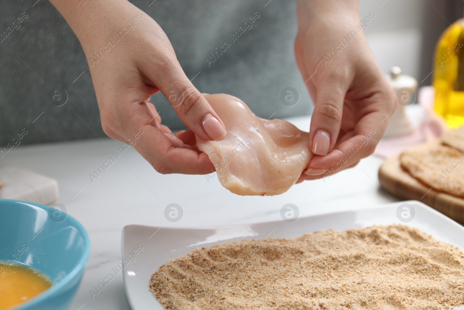 Photo of Woman making schnitzel at white table, closeup