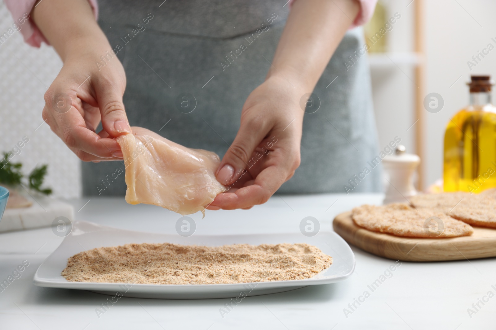 Photo of Woman making schnitzel at white table, closeup