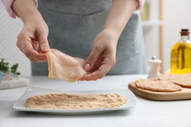 Woman making schnitzel at white table, closeup