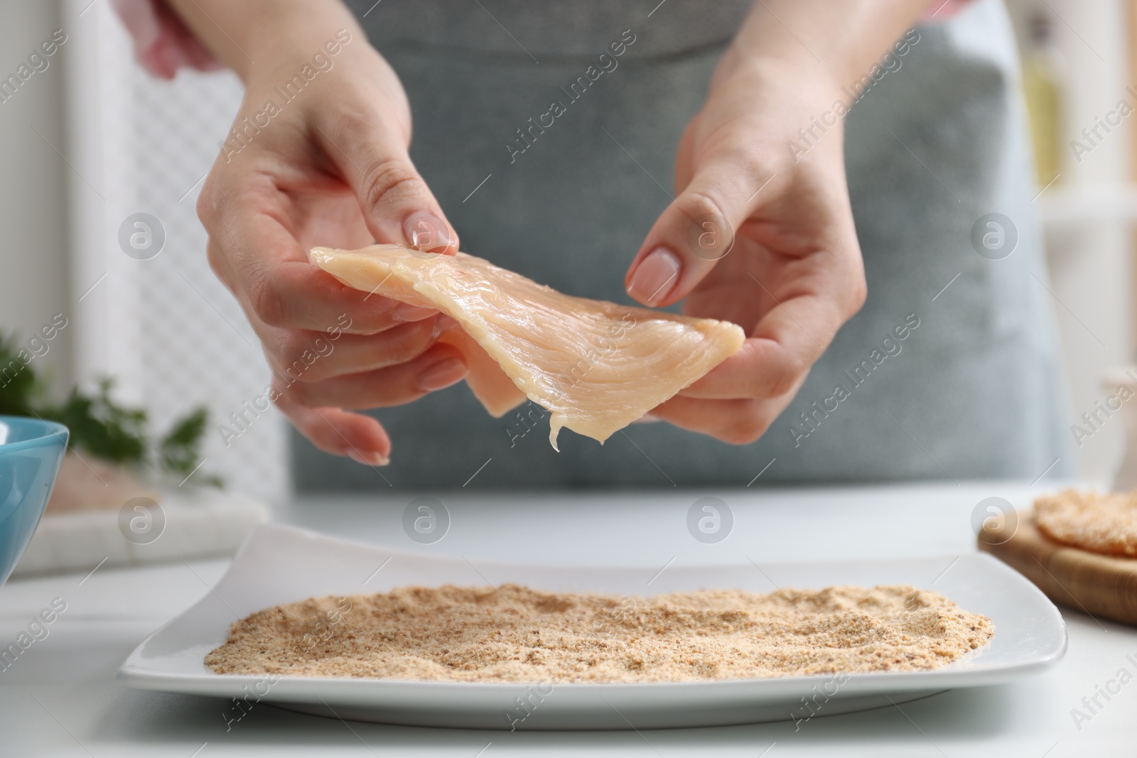 Photo of Woman making schnitzel at white table, closeup