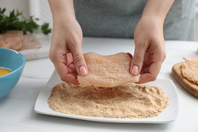 Woman making schnitzel at white table, closeup