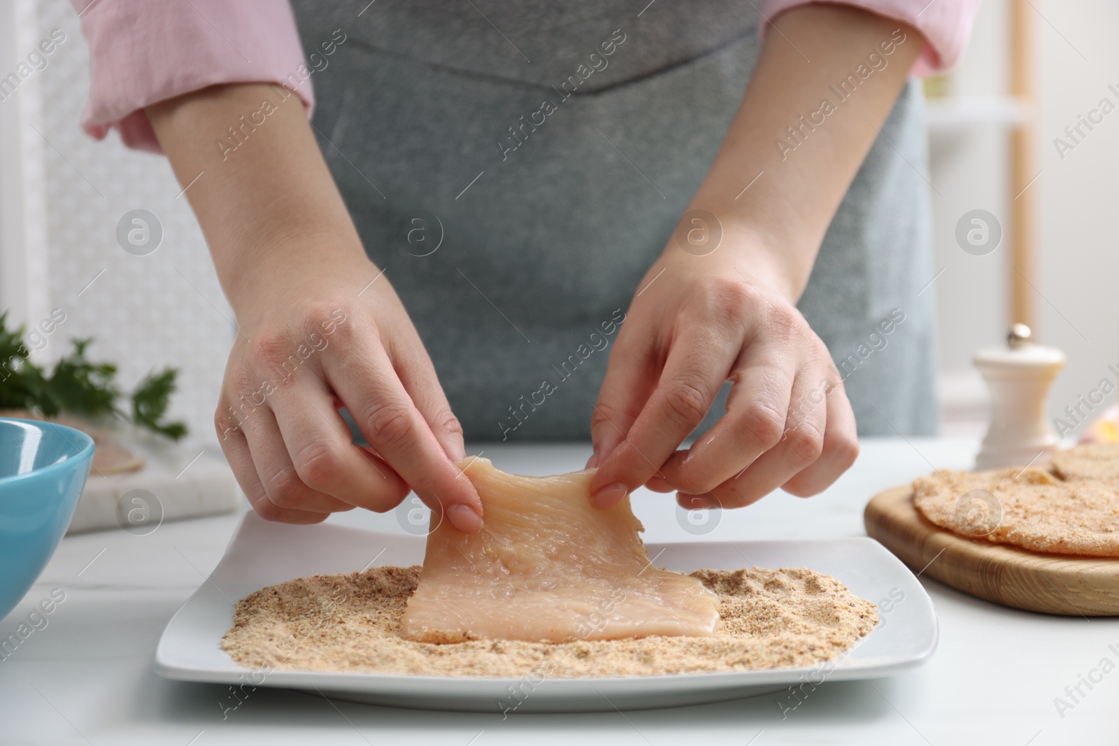 Photo of Woman making schnitzel at white table, closeup