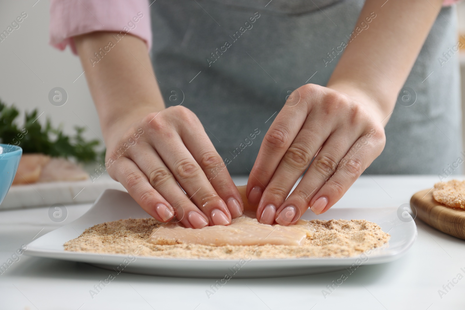 Photo of Woman making schnitzel at white table, closeup