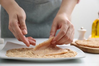 Photo of Woman making schnitzel at white table, closeup