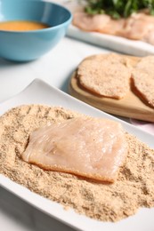 Making schnitzels. Raw meat with breadcrumbs on white marble table, closeup