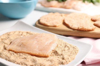 Photo of Making schnitzels. Raw meat with bread crumbs on table, closeup