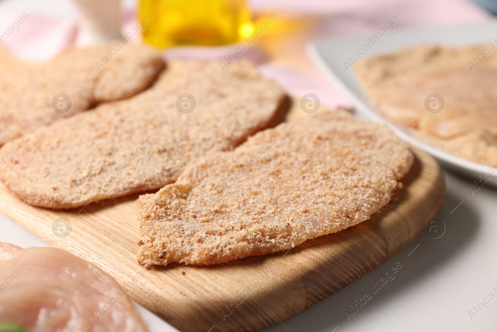 Photo of Making schnitzels. Raw meat with breadcrumbs on white marble table, closeup