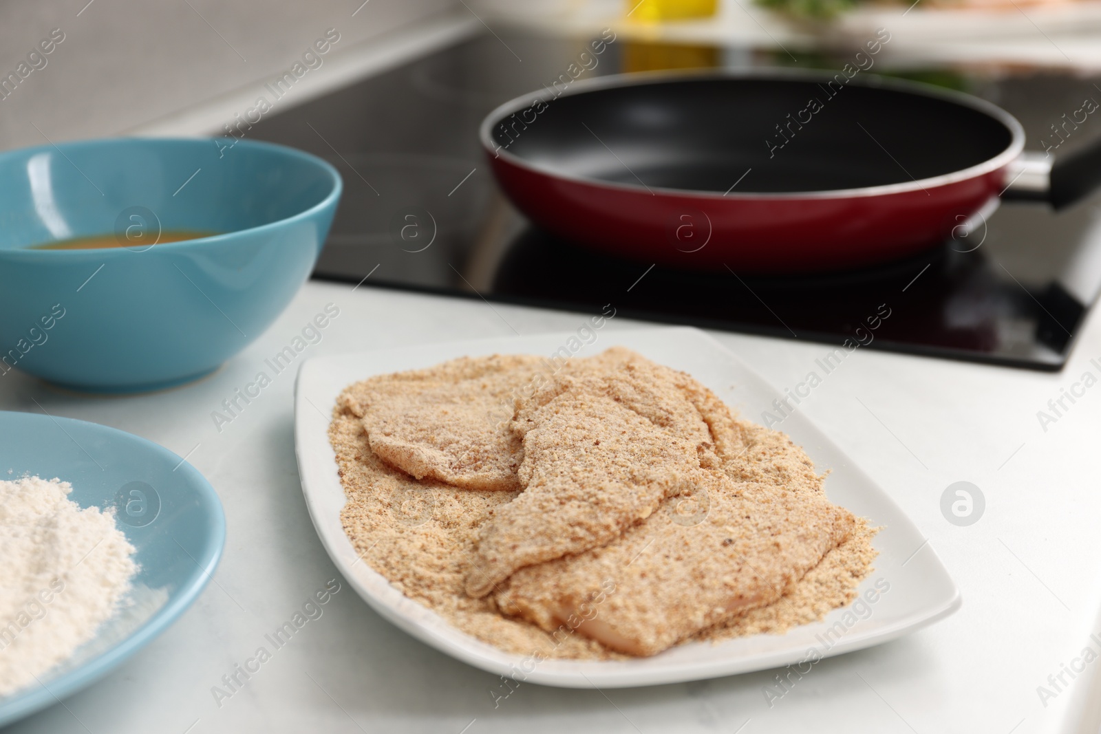 Photo of Making schnitzels. Raw meat with bread crumbs on white table, closeup