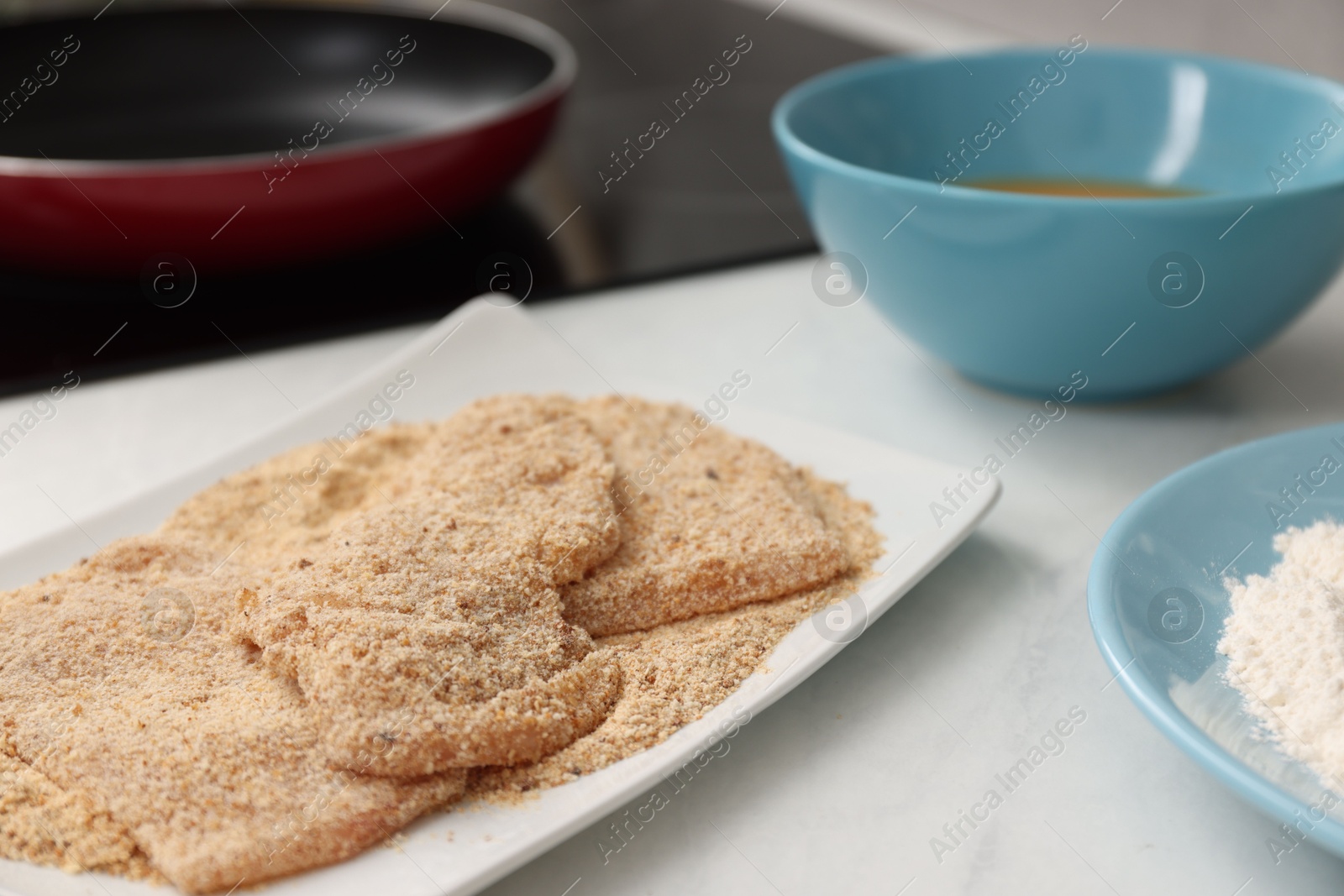 Photo of Making schnitzels. Raw meat with bread crumbs on white table, closeup