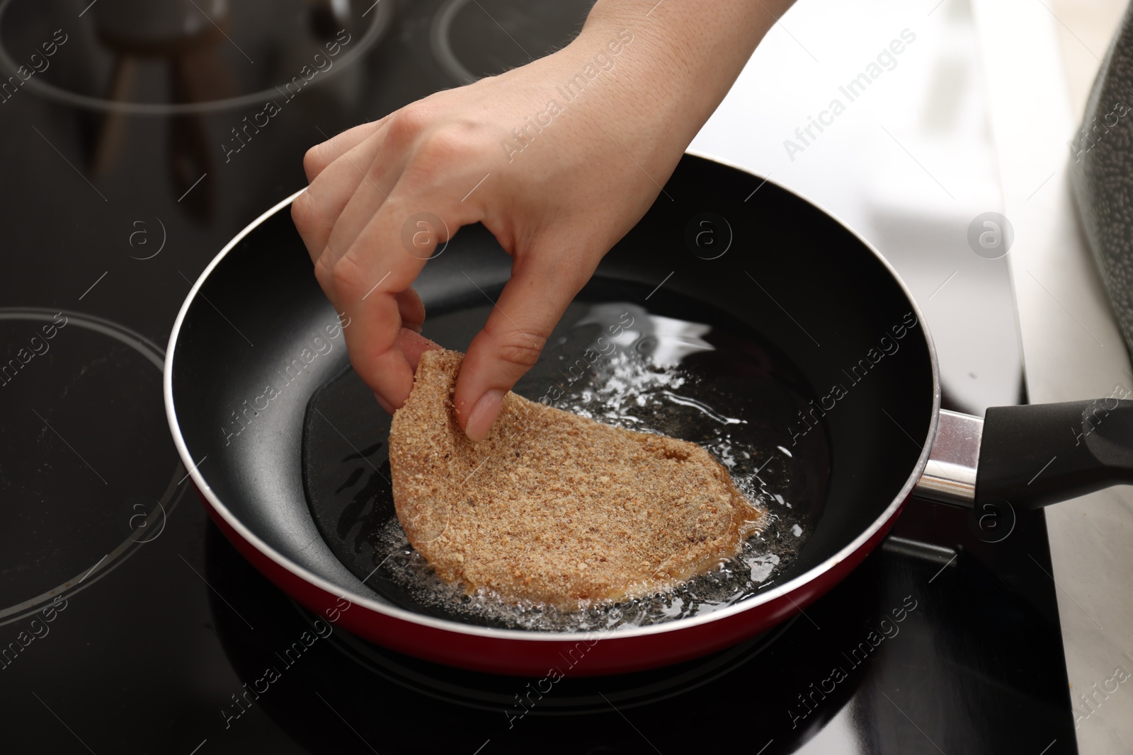 Photo of Woman cooking schnitzel in frying pan on stove, closeup