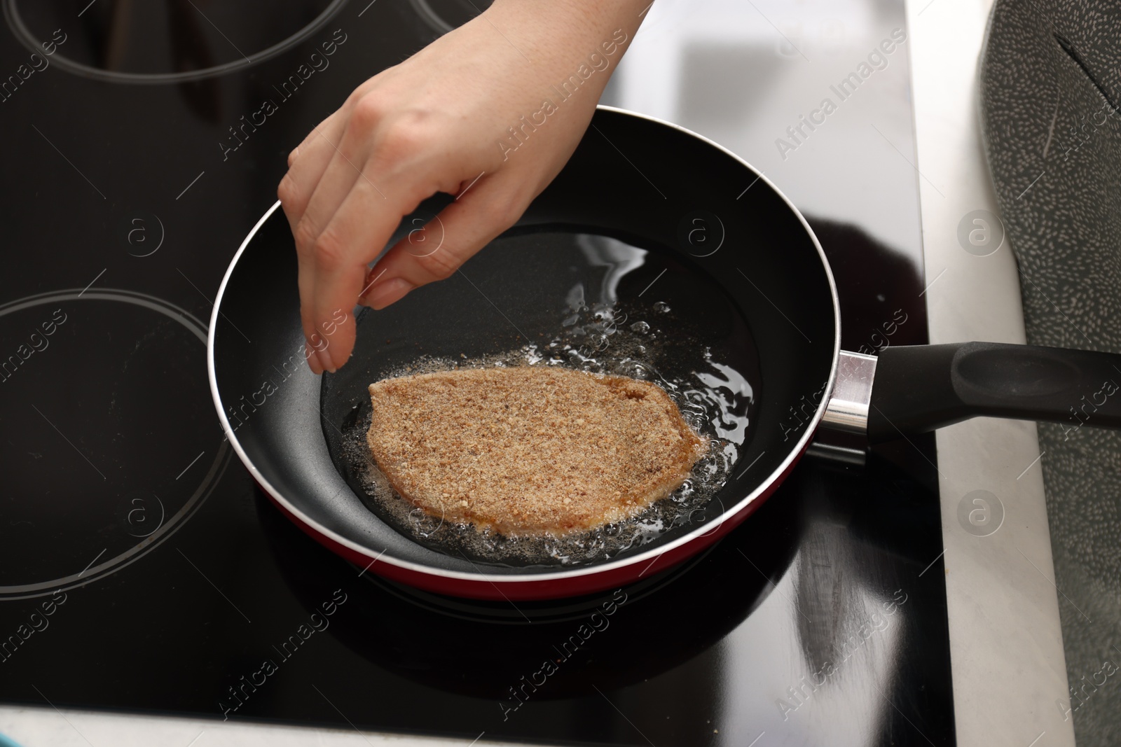 Photo of Woman cooking schnitzel in frying pan on stove, closeup