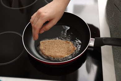 Woman cooking schnitzel in frying pan on stove, closeup