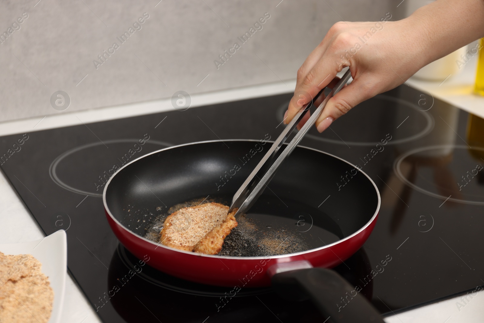 Photo of Woman cooking schnitzel in frying pan on stove, closeup