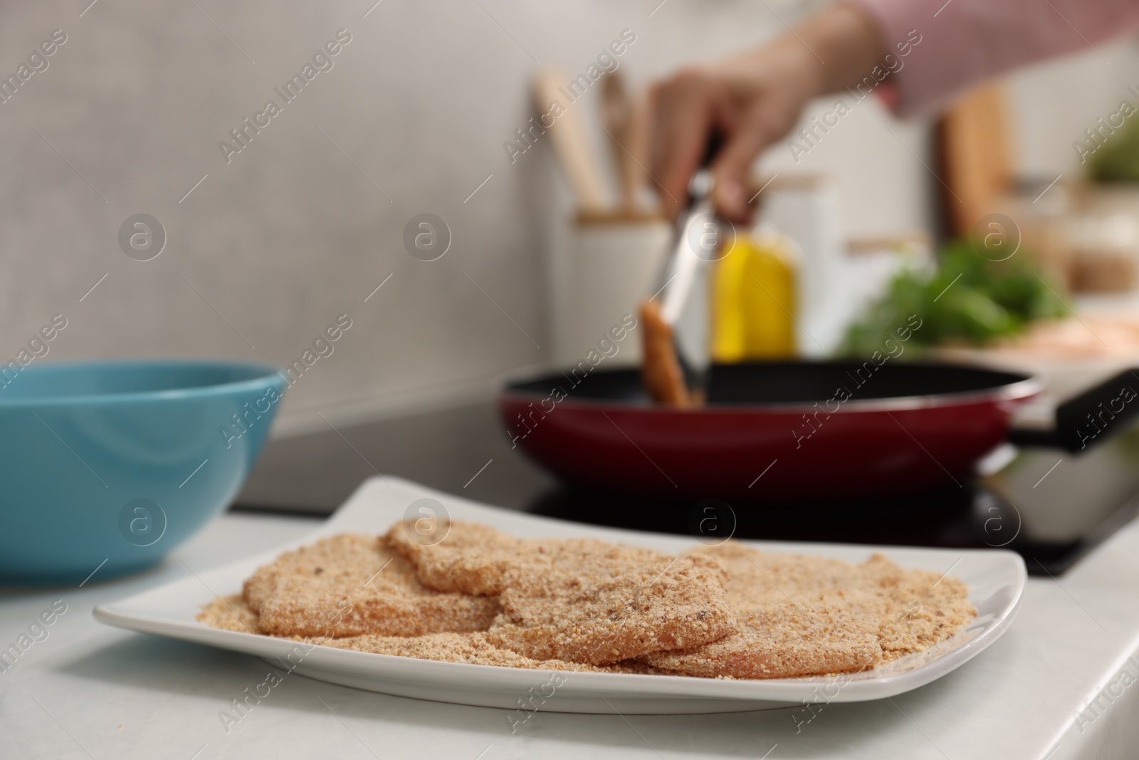 Photo of Woman cooking schnitzels in frying pan on stove, focus on raw meat with breadcrumbs