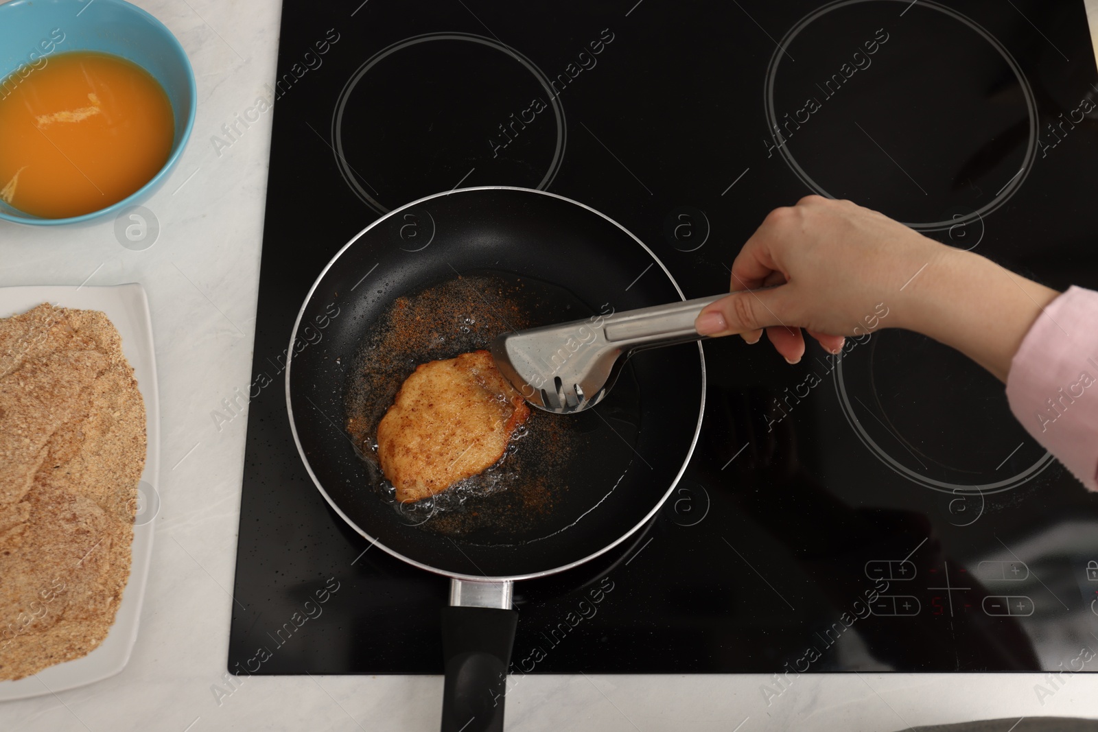 Photo of Woman cooking schnitzel in frying pan on stove, top view