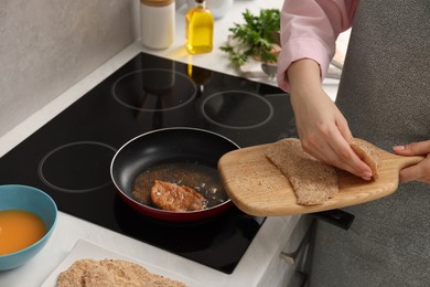 Woman cooking schnitzel in frying pan on stove, closeup