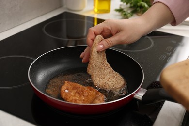 Photo of Woman cooking schnitzels in frying pan on stove, closeup