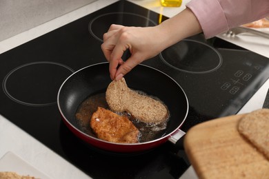 Woman cooking schnitzels in frying pan on stove, closeup