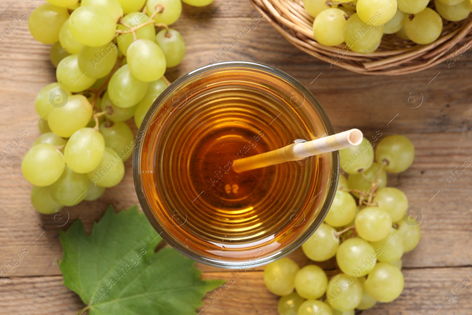 Photo of Tasty juice in glass, fresh grapes and leaf on wooden table, top view